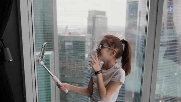 Modern Teenage Girl Taking a Selfie Near the Window in a Modern Apartment Overlooking the City From