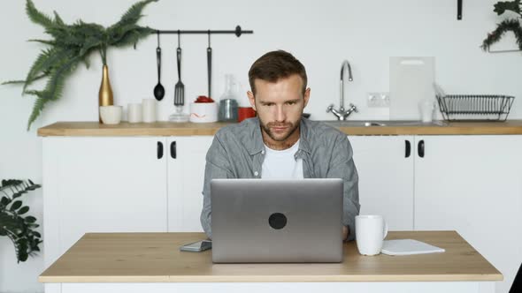 A Young Thoughtful Freelance Man Looking at A Monitor Screen, Working at a Computer