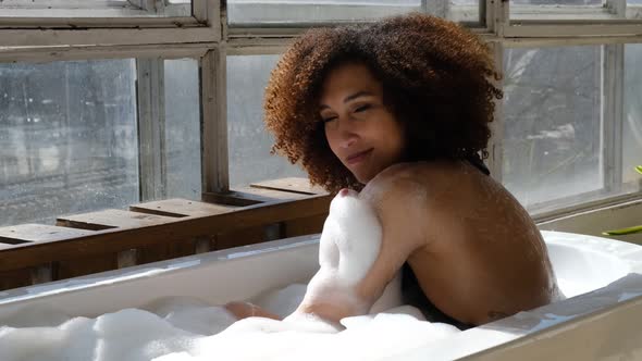 Smiling and Relaxing African American Woman Bathing in a Tub Full of Foam