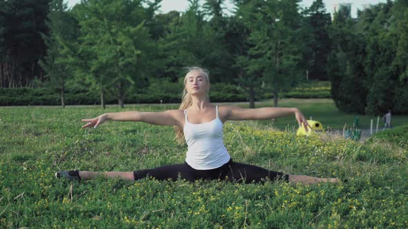 Blonde Girl Sits on a Hill and Doing the Exercises Right and Left Turns