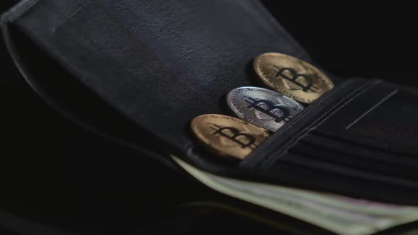 Bitcoin and Paper Currency Are in a Black Wallet. Black Background. Close-up