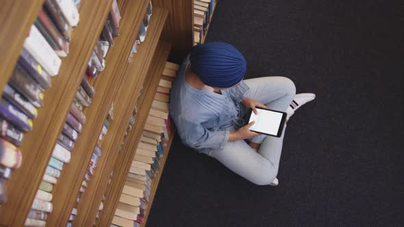 Asian female student wearing a blue hijab sitting on the floor and using tablet