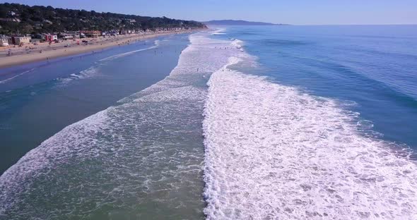 Aerial footage along a Pacific shore in Southern California. People are swimming and surfing in the