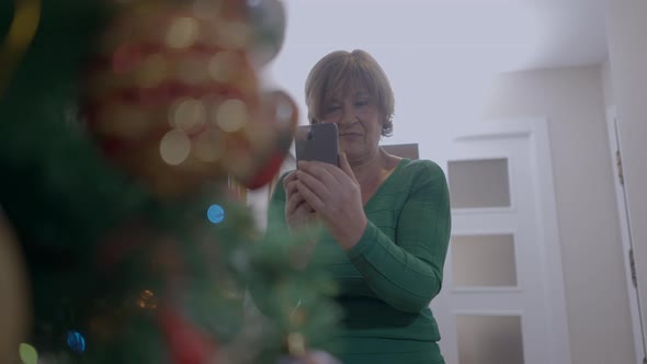 Female Pensioner In The House Capturing Photo Of Glittering Christmas Tree With Cellphone Camera