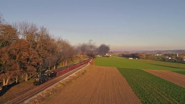 Aerial View of an Antique Steam Locomotive Approaching Pulling Passenger Cars and Blowing Smoke and Steam During the Golden Hour in late Afternoon
