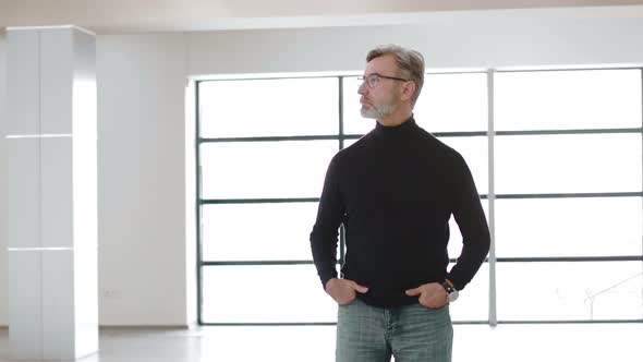 Confident Caucasian adult man in a black turtleneck and glasses, stands against the background
