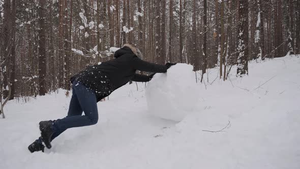 Caucasian Man Rolls Large Snow Globe with Effort