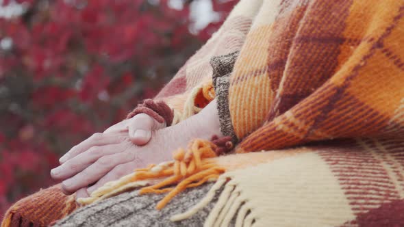 Hands of an Elderly Woman Who Sits in a Blanket Against the Backdrop of an Autumn Landscape