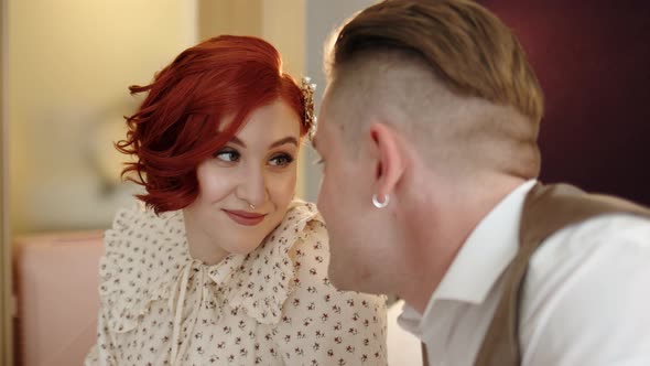 Couple of Man and Woman in Costumes Sit on Bed in Hotel or Apartment and Chat Looking Into Their