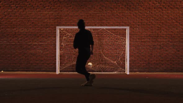 Young Man Playing Football on the Playground at Night - Kicking Ball in Gates