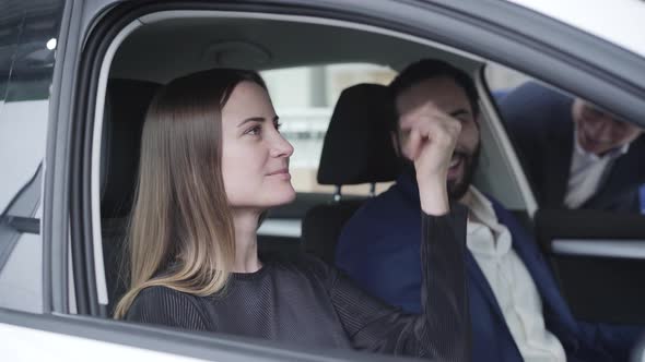 Young Beautiful Caucasian Woman Sitting on Passenger Seat in Car and Talking with Middle Eastern Man