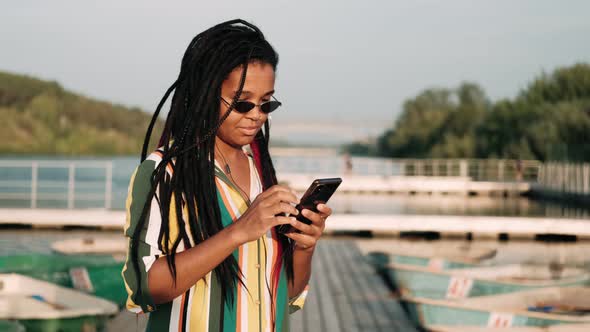 Beautiful AfricanAmerican Girl in Sunglasses Looks at the Phone Chats in Messengers Answers Messages