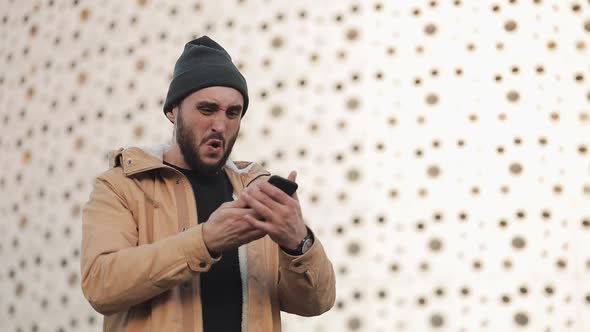 Young Man Reading Bad News on Smartphone Standing Near Office Center. He Looks Shockes and Worried