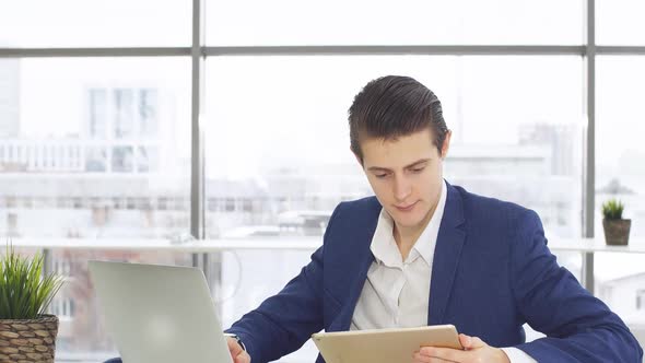 Young Businessman Sitting By Table with Laptop and Looking in Camera.