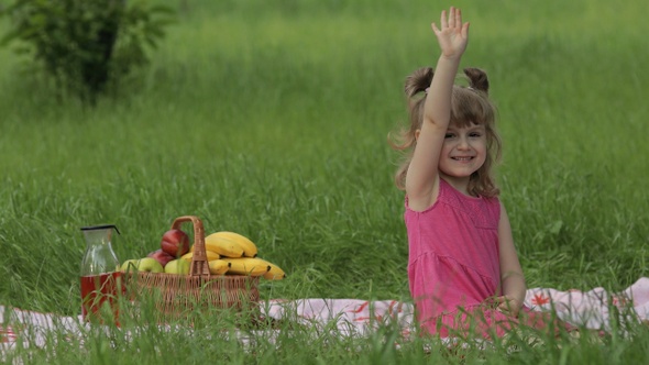 Weekend at Picnic. Lovely Caucasian Child Girl on Green Grass Meadow Sit on Blanket Waving Her Hands