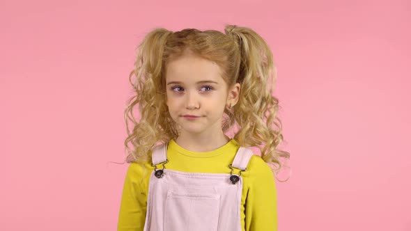 Blond Child Pursing Her Lips, Having Thoughtful Playful Face Is Turning Her Head and Rolling Her