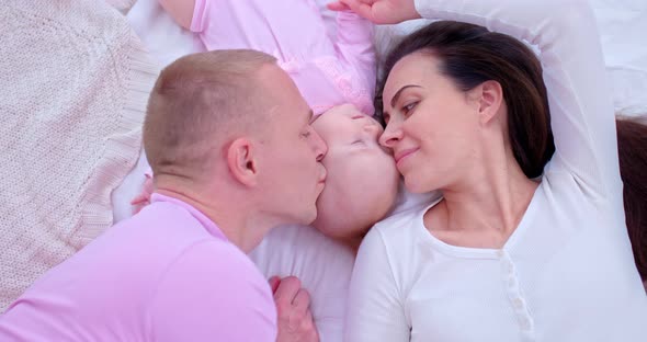 Portrait, Young and Loving Mom and Dad Kiss Their Baby Daughter on the Cheeks. Beautiful Mom, Dad