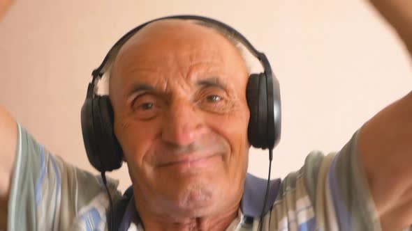 Happy Caucasian pensioner in headphones dances and listens to music. Home leisure of an elderly pers