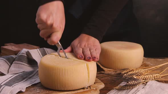 Women cut a wheel of  fresh homemade cheese on a wooden board with a cheese knife close up