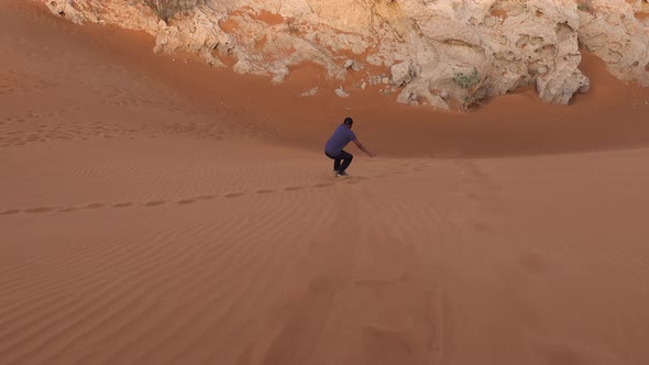 Male Tourist Sand Boarding Down Desert Dune In Dubai