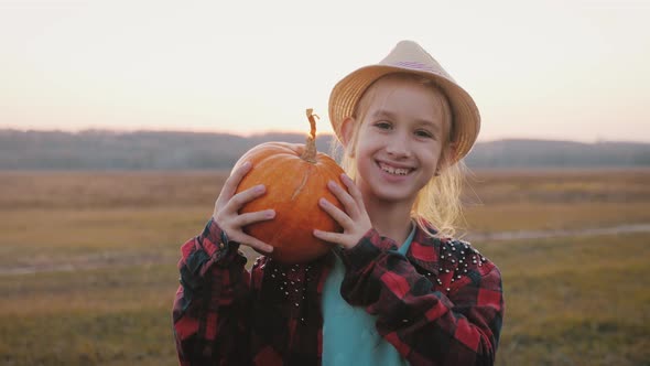 Young Girl Farmer in Hat Holding Orange Pumpkin in Her Hands the at Field at Sunset Time. Pumpkin