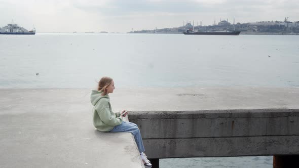 Child with Smartphone Sitting on Sea Pier and Swaying Legs