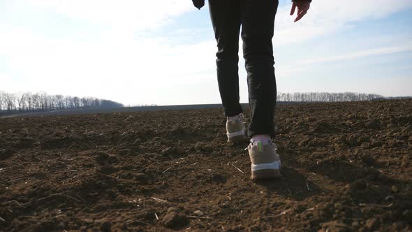 Rear View of Little Girl in Jacket Walks on the Dry Ground Along Ploughed Meadow at Sunny Day