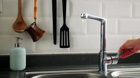 Hands of woman turning faucet on and off in the kitchen.