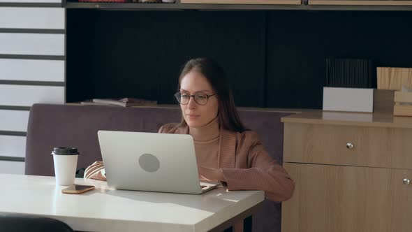 Beautiful woman in eyeglasses use laptop and drink coffee in coffee shop.