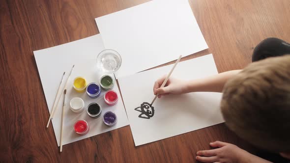 Top view of child painting with gouache sitting on floor at living room. Creativity concept.