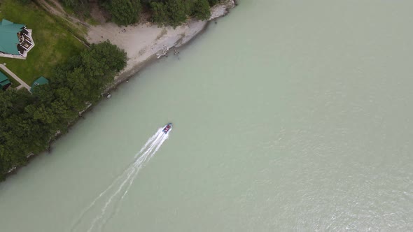 A Blue Inflatable Boat with Passengers is Dusting Along the Sandy Shore with Green Trees