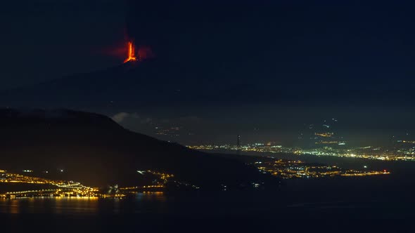 Timelapse of eruption of Mount Etna volcano at night time with sea and city lights in foreground see