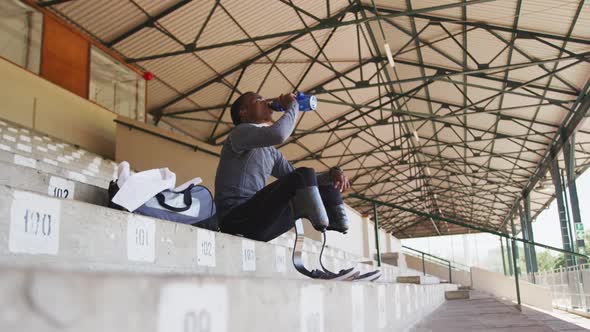 Disabled mixed race man with prosthetic legs drinking water and looking away