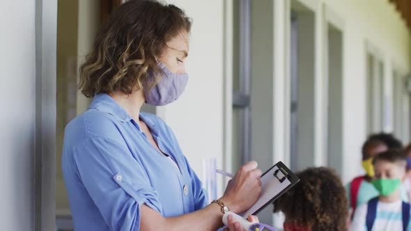 Female teacher wearing face mask writing on clipboard