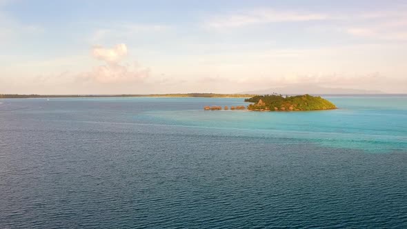 drone flight over the ocean in front of Bora Bora. Different blues in the water, small Motu / Island