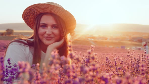 Beautiful Young Girl in a Straw Hat and White Dress Sitting in a Lavender Field on Sunset