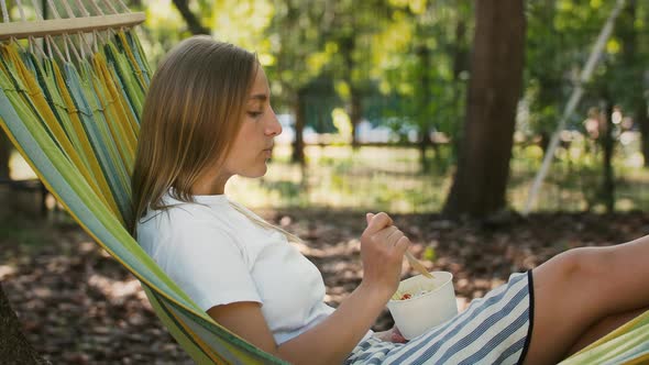 Young Model Having a Rest Lying in Colorful Hammock and Eating Ice Cream