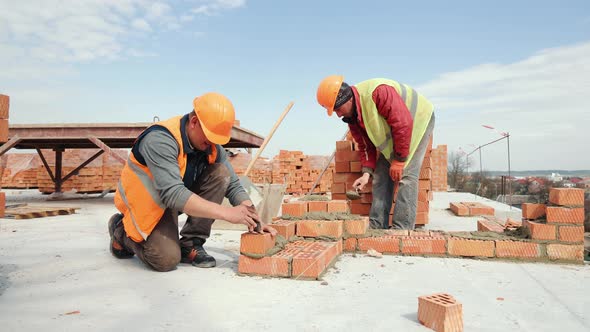 Two Builders Laying a Brick Wall on the Construction of a Multistorey Building