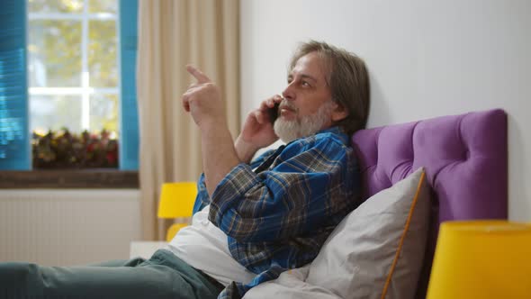 Happy Senior Man Talking on Mobile Phone in Bedroom at Home