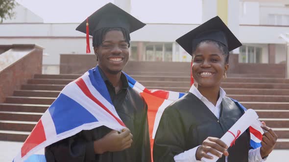 African American Man and Woman Stand Side By Side Facing the Camera in Black Robes and Square Hats