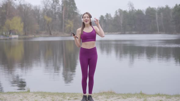 Wide Shot of Sportive Brunette Woman in Purple Sportswear and Headphones Listening To Music