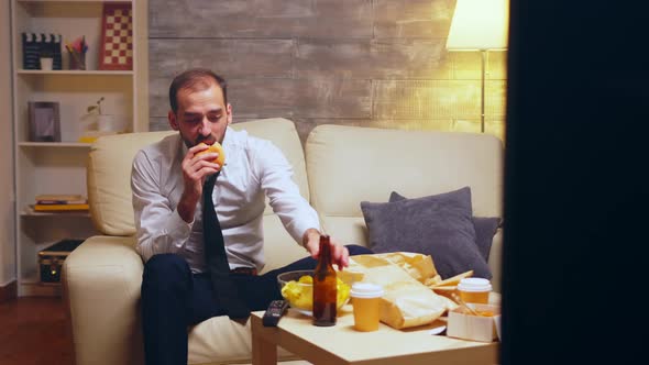 Businessman with Tie Sitting on Couch Eating a Burger