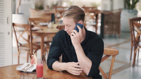 Portrait of Businessman in Black Shirt Sitting in Cafe and Talking on Phone