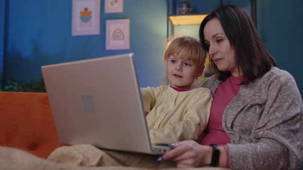 Mother and Small Child Daughter Kid Study at Laptop Watching Funny Movies Relaxing Lying on Sofa