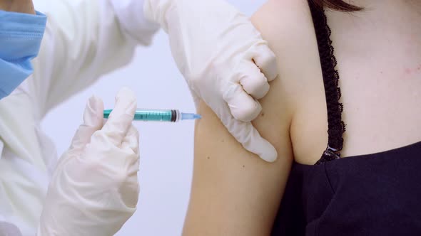 A Medical Nurse Wearing Protective Gloves and a Protective Mask Gives a Vaccine Injection To a