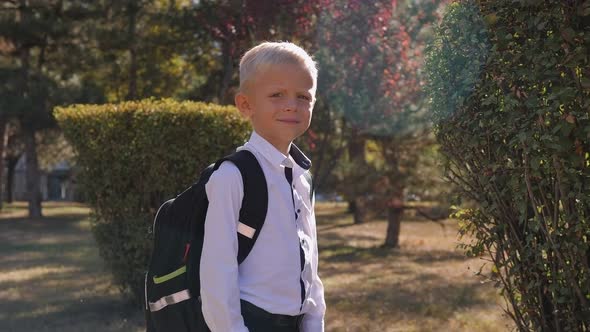 Small Schoolboy with His Arms Crossed Over His Chest with a Backpack in the Park