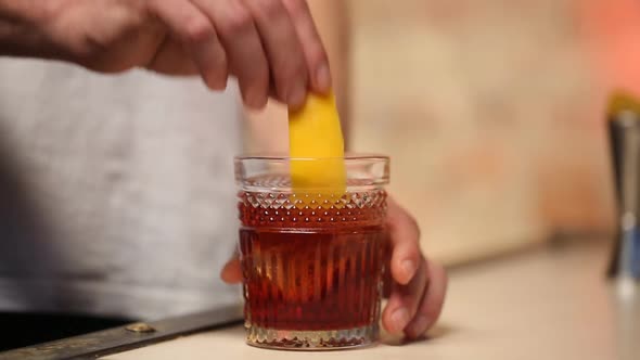 The Bartender Holds the Zest of Orange Along the Edge of the Glass with a Cocktail