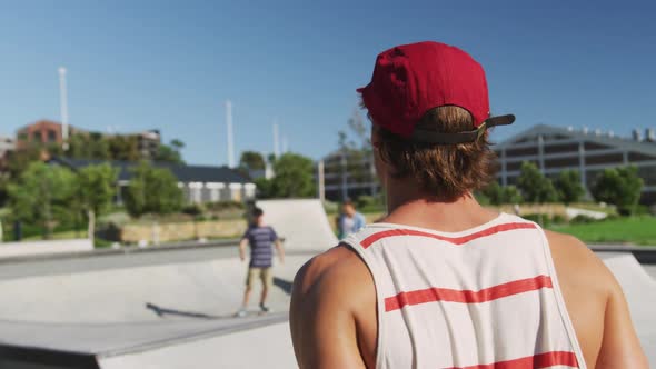 Portrait of smiling caucasian man turning back on sunny day, skateboarders in background