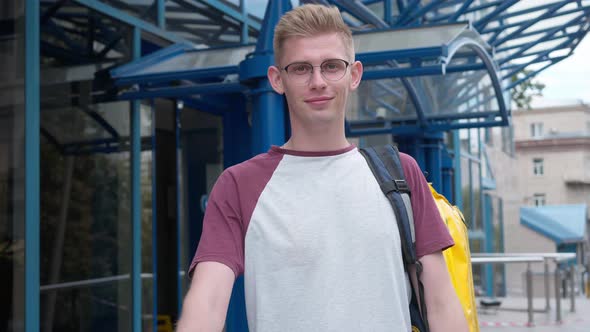 Portrait of Handsome Young Caucasian Courier Looking at Camera Stretching Food Delivery Package