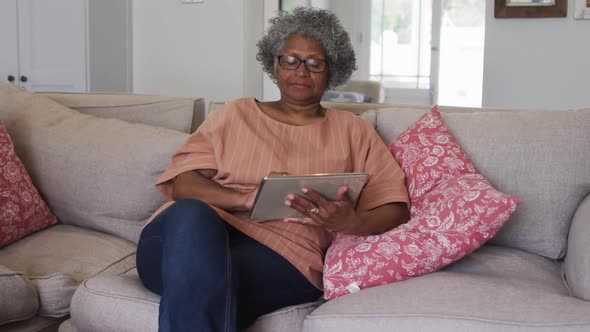 Senior african american woman using digital tablet while sitting on the couch at home